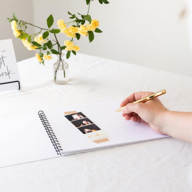 Hand holding gold pen about to write in open guestbook next to a polaroid photo